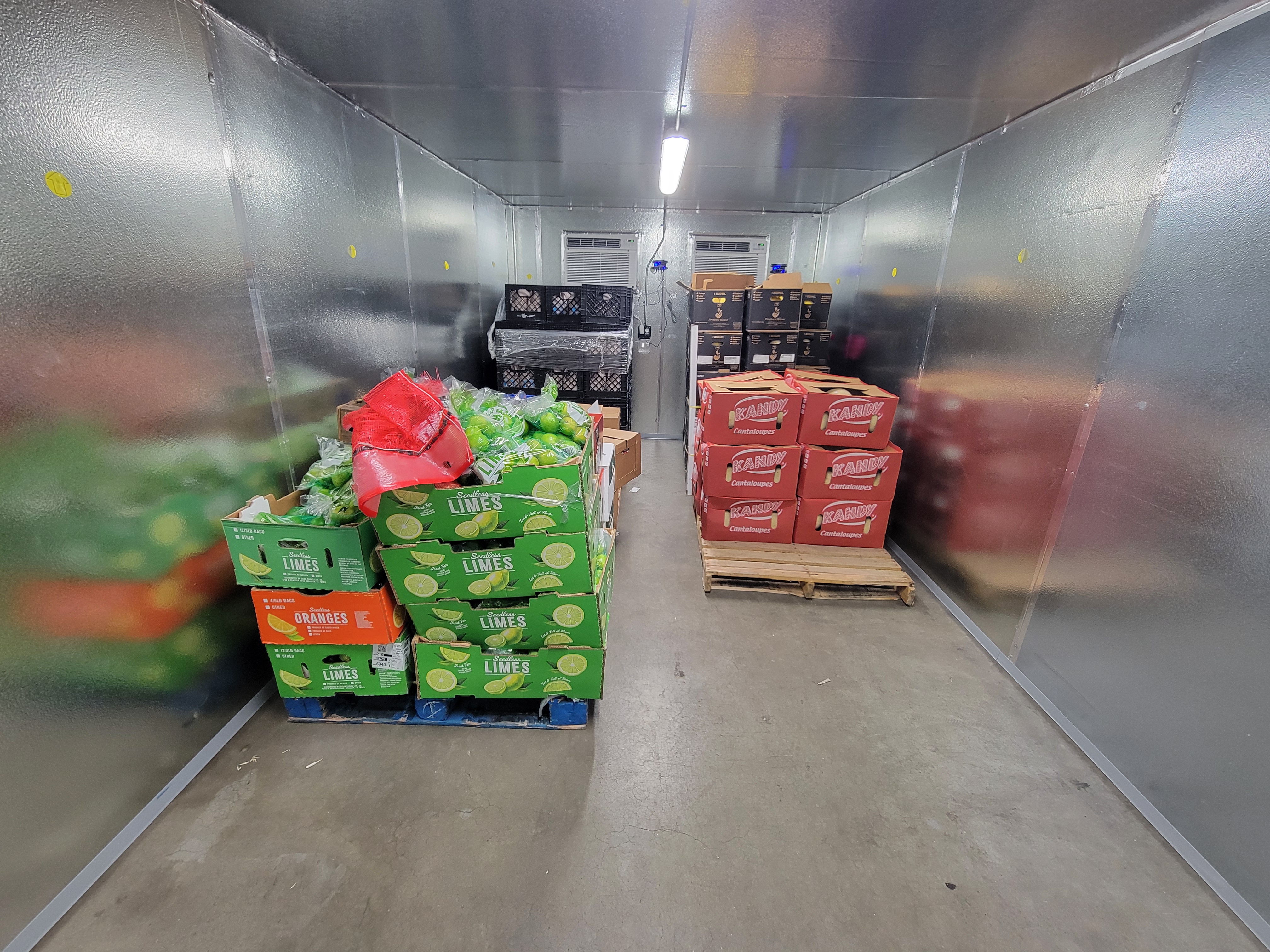 Pallets of cardboard boxes filled with different produce in fridge box unit.